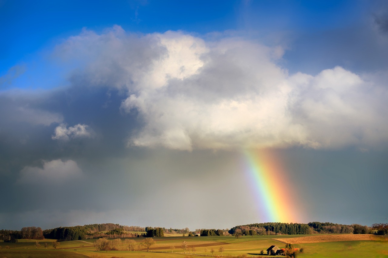 Plains with clouds below a bit of blue sky with a rainbow coming down from the clouds.