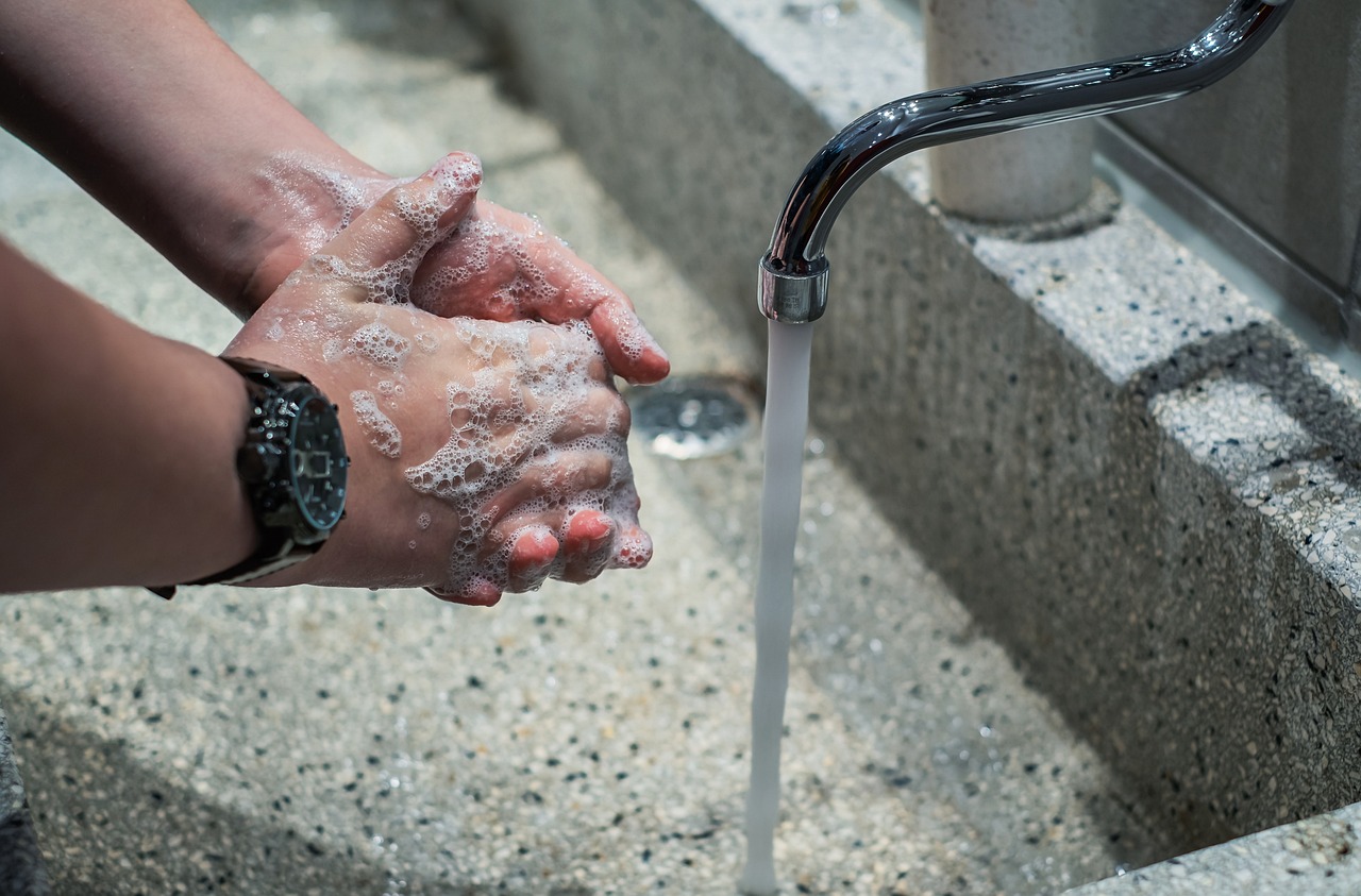 A person wearing a watch soaps their hands over a sink into which water is runing from a faucet.
